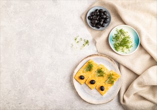 Marble cheese with olives and watercress microgreen on gray concrete background and linen textile.