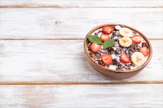Chocolate cornflakes with milk and strawberry in wooden bowl on white wooden background. Side view,