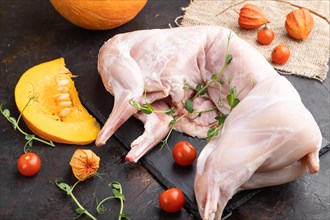 Whole raw rabbit with pumpkin, tomatoes, pea sprouts on a black concrete background and linen