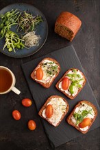Red beet bread sandwiches with cream cheese, tomatoes and microgreen on black concrete background.