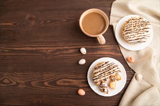 Tartlets with meringue cream and cup of coffee on brown wooden background and linen textile. top