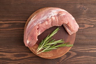 Raw pork with herbs and spices on a wooden cutting board on a brown wooden background. Top view,