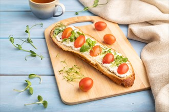 Long white bread sandwich with cream cheese, tomatoes and microgreen on blue wooden background and