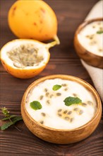 Yoghurt with granadilla and mint in wooden bowl on brown wooden background and linen textile. side