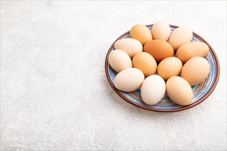 Pile of colored chicken eggs on plate on a gray concrete background. side view, copy space, close