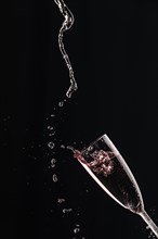 Drops and splashes fly from a champagne glass with rose sparkling wine on a black background