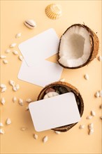 White paper business card with coconut and seashells on orange pastel background. Top view, flat