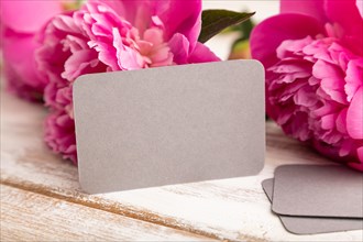 Gray business card with pink peony flowers on white wooden background. side view, copy space, still