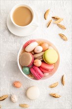 Multicolored macaroons and chocolate eggs in ceramic bowl, cup of coffee on gray concrete