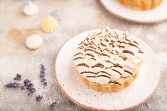 Two tartlets with meringue cream and cup of coffee on brown concrete background. side view,