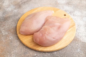 Raw chicken breast on a wooden cutting board on a brown concrete background. Side view, close up