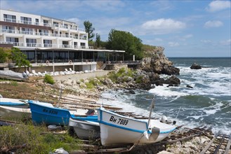 A coastal hotel overlooking the moving sea, surrounded by boats and rocky landscape, harbour and