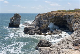 Rocky coastal landscape with a natural arch over a roaring sea under a clear blue sky, rock arch,