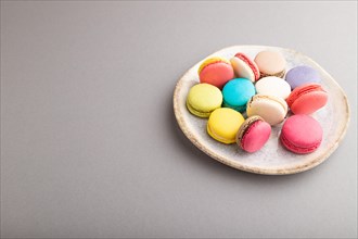 Multicolored macaroons on ceramic plate on gray pastel background. side view, close up, still life,