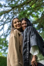 Vertical image of two female friends together happily looking at the camera with tree branches