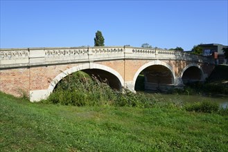 A brick arch bridge over a small river in the countryside under a clear blue sky, Baroque Art