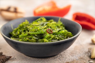 Chuka seaweed salad in blue ceramic bowl on brown concrete background. Side view, close up,