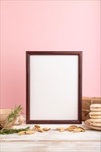 Brown wooden frame mockup with cup of coffee, almonds and macaroons on pink pastel background.