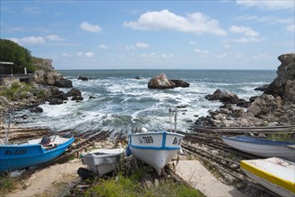 Boats on a coastline with rough seas and rocky outcrops in the background, harbour, Tyulenovo,
