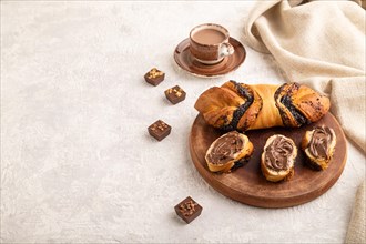 Homemade sweet bun with chocolate cream and cup of coffee on a gray concrete background and linen