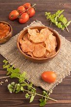 Slices of dehydrated salted meat chips with herbs and spices on brown wooden background and linen