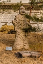 Stone carved statue of Buddhist deity kanakavatsa in front of white wall in garden in South Korea