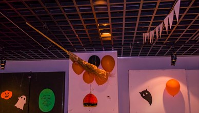 Wooden wicker broom hanging from ceiling with orange balloons and hand made Halloween decorations