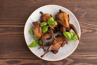 Smoked quails with herbs and spices on a ceramic plate on a brown wooden background. Top view, flat