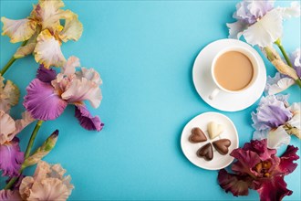 Cup of cioffee with chocolate candies, lilac and purple iris flowers on blue pastel background. top