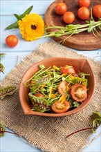 Vegetarian vegetables salad of tomatoes, marigold petals, microgreen sprouts on blue wooden