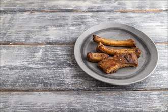 Pork ribs on a wooden plate on a gray wooden background. Side view, close up, copy space