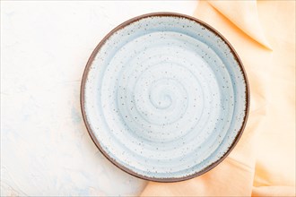 Empty blue ceramic plate on white concrete background and orange linen textile. Top view, close up,