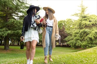 Front view of a lesbian couple walking in the park with a bottle of champagne and glasses to
