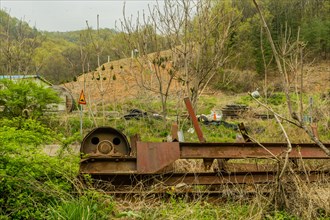 Rusting frame and motor of old conveyor belt laying in tall weeds in wilderness on mountainside