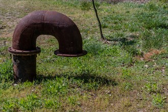 Curved iron vent pipe protruding from lush grass covered ground in wilderness