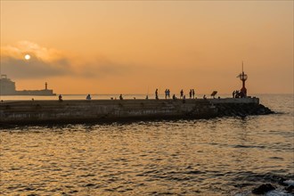 Unidentified people fishing of concrete pier at sunset in Jeju, South Korea, Asia