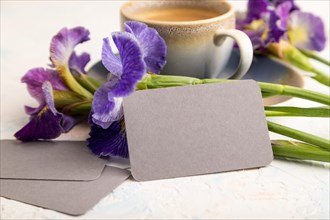 Gray business card with cup of cioffee and iris flowers on white concrete background. side view,