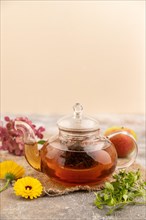 Red tea with herbs in glass teapot on brown concrete background and linen textile. Healthy drink