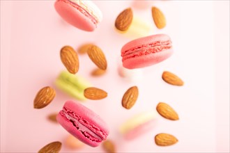 Multicolored flying macaroons and almonds frozen in the air on blurred pink background. top view,