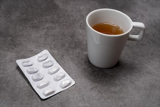 A blister pack with pills next to a cup of tea on a grey background, top view, studio shot,