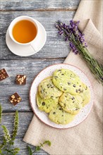 Green cookies with chocolate and mint on ceramic plate with cup of green tea and linen textile on