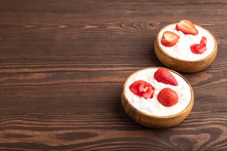Grained cottage cheese with strawberry jam on brown wooden background. side view, copy space