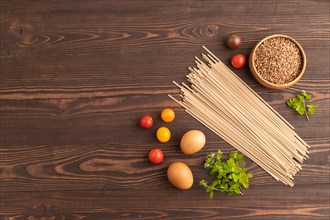 Japanese buckwheat soba noodles with tomato, eggs, spices, herbs on brown wooden background. Top