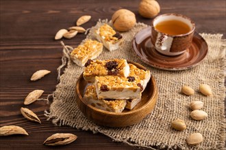Traditional candy nougat with nuts and sesame with cup of green tea on brown wooden background and