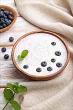 Yogurt with blueberry in wooden bowl on white wooden background and linen textile. Side view, close