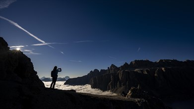 Mobile phone photographer on ridge with Dolomites mountains in the background, Corvara, Dolomites,