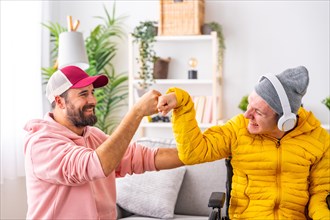 Disabled man and friend feeling happy and giving each other a fist bump while listening to music at