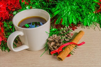 Cup of black coffee in a white cup next to pine cones and cinnamon stick with red and green