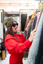 Vertical photo of an amazed woman trying on and shopping second hands vintage clothes during sales