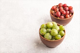 Fresh red and green gooseberry in clay bowl on gray concrete background. side view, copy space